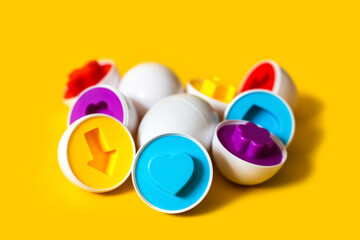 Multicolored plastic eggs on yellow background. An educational sorter toy for toddler to recognize and match colors and shapes. Puzzle montessori game concept. Closeup, copy space for text