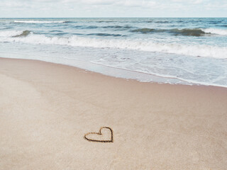 Fototapeta na wymiar Sea coast with soft surf. Heart drawn on sandy beach. International symbol of love and romance. Vacation on seaside.