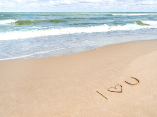 Sea coast with soft surf. Words I LOVE YOU and heart symbol written on sandy beach. Vacation on seaside.