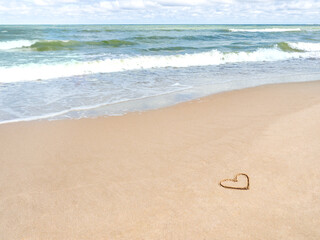 Sea coast with soft surf. Heart drawn on sandy beach. International symbol of love and romance. Vacation on seaside.