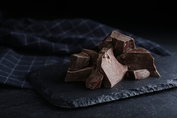 Pieces of tasty dark chocolate on black table