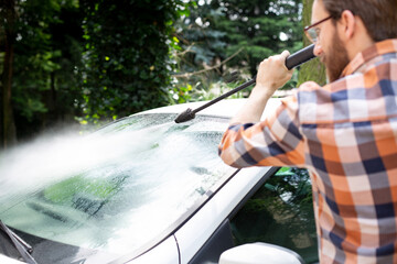 Man cleaning a car in the garden with a compact high pressure washer .