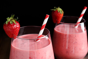 Tasty strawberry smoothies in glasses on black background, closeup