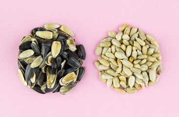 Two round piles of roasted peeled sunflower seeds and husk on puple pink background.