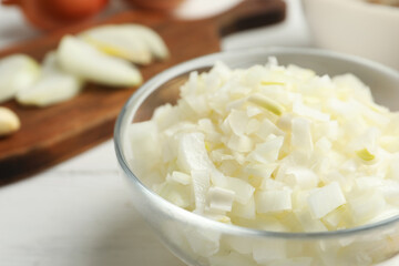 Chopped onion in bowl on white wooden table, closeup