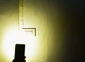 flashlight of mobile phone spreading light  to electric switch on home wall while power outage in...