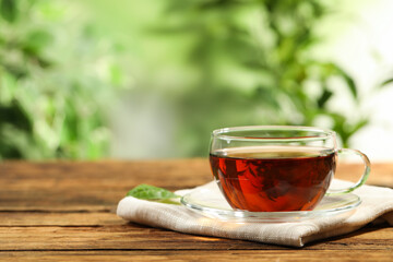 Cup of black tea on wooden table against blurred background. Space for text