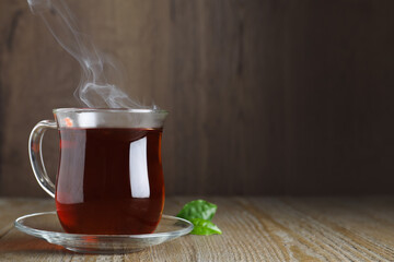 Glass cup of aromatic black tea on wooden table, space for text