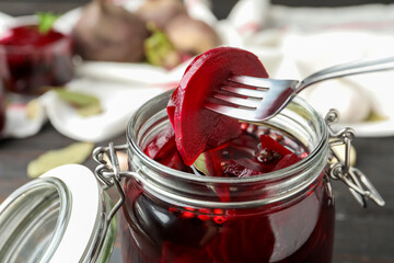 Fork with pickled beets over glass jar on wooden table, closeup