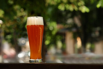 Glass of tasty beer on railing outdoors, space for text