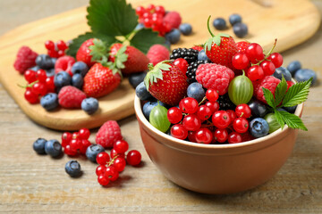 Mix of different fresh berries in bowl on wooden table