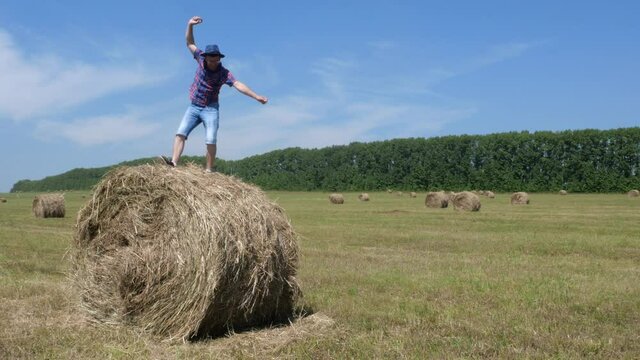 A man in a hat and glasses is dancing on a bale of hay.
