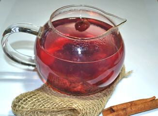 Hot cherry tea in the glass teapot on jute with cinnamon stick  isolated against white grey background. Fruit tea collection. Healthy breakfast. 