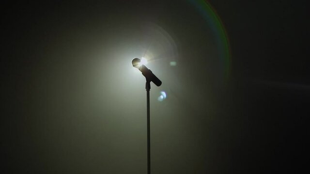 Close-up of microphone on stage against a black background with white lighting and smoke. The silhouette of the microphone in the dark. Music instrument concept.
