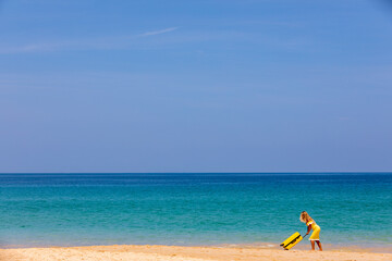 Beautiful girl in a swimsuit on the beach with a yellow suitcase. Blue sea. Yellow sand