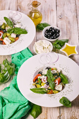 Greek salad. Mediterranean vegetable salad with fresh basil, olives, olive oil and spices. Food still life composition on a wooden table. Vertical shot