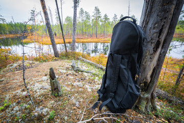 Long black closed bag backpack for gun stands on forest bank on background of river in autumn.