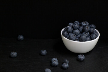 Blueberries with mint leaves in a small white bowl. On a black granite board. Wood background.