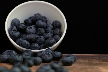 Blueberries with mint leaves in a small white bowl. On a black granite board. Wood background.