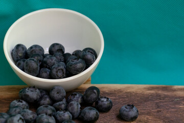 Blueberries scattered from a small white bowl. On a dark wooden background.