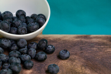 Blueberries scattered from a small white bowl. On a dark wooden background.