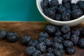 Blueberries scattered from a small white bowl. On a dark wooden background.