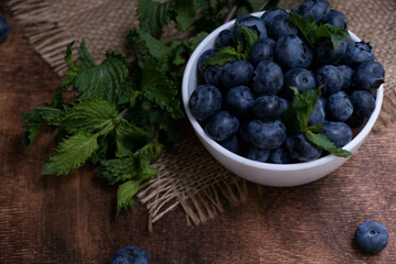 Blueberries with mint leaves in a small white bowl. On a black granite board with a cloth napkin. Wood background.