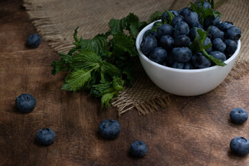 Blueberries with mint leaves in a small white bowl. On a black granite board with a cloth napkin. Wood background.