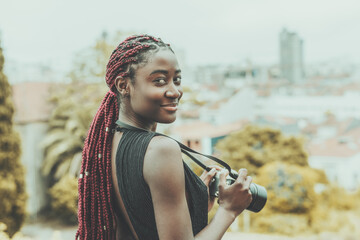 A dazzling young African tourist woman photographer with maroon colored braids is staying on some...