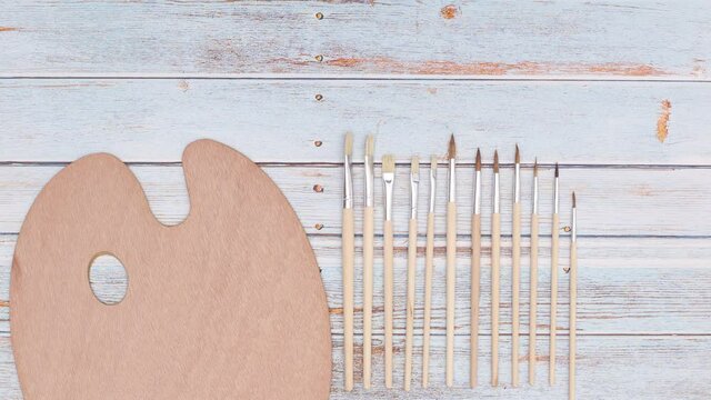 Artist palette and painting brushes appear on wooden table. Stop motion animation 