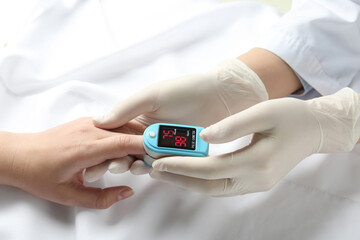 Doctor examining patient with fingertip pulse oximeter in bed, closeup