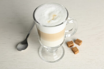 Delicious latte macchiato and sugar cubes on white table, closeup