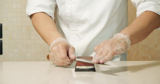 Chef hands sharpening knife in slow motion. Closeup man hands preparing professional tools for cooking food at kitchen restaurant.