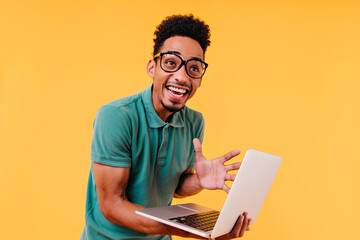 Laughing black man in glasses expressing excitement on yellow background. Studio photo of emotional...