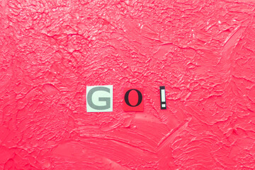  cut out letters and composed word GO! on blurred pink background 