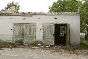 Old white abandoned dilapidated brick garage with wooden green gate doors.  A two-car garage on the territory of a state-owned enterprise.
