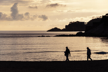 Two persons walking on the shore of Mediterranean Sea at sunset
