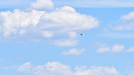 Small airplane flies among the white clouds on the blue sky