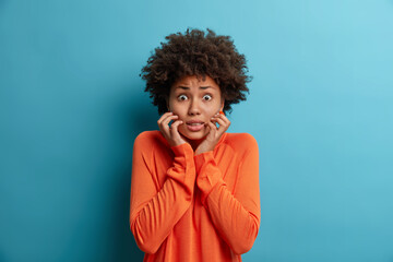 Photo of nervous scared woman grabs face and looks with worried expression at camera, sees phobia,...