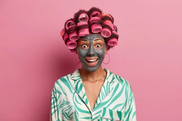 Deurstickers Happy joyful woman visits hairdressing and spa salon, makes perfect hairstyle and applies clay face mask, wears pyjama, has surpised expression, isolated on pink background. Female going on date © Wayhome Studio
