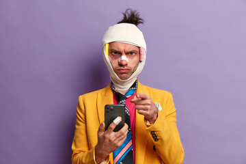 Strict displeased man with bandage wrapped around head, points at you and expresses negative...