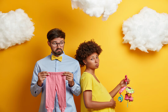 Photo of tired pregnant wife poses together with husband, holds mobile and touches tummy, looks sadly at camera. Married family couple prepare for parenthood, expect child. Child birth concept