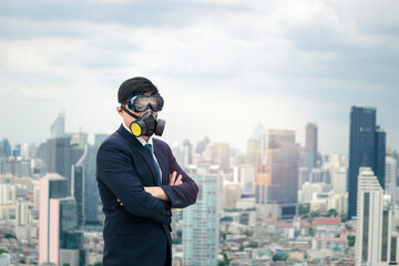 Asian young businessman in suit wearing chemical protective face mask, crossing his arms with skyscraper city, air pollution problem in city concept