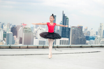 Asian ballerina dancer girl practicing ballet dancing on rooftop with skyscraper city view, adorable child dancing in ballet