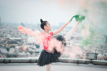 Asian ballerina dancer girl practicing ballet dancing with  colored smoke bomb on rooftop with skyscraper city view, adorable child dancing in ballet