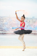 Fototapeta na wymiar Asian ballerina dancer girl practicing ballet dancing with colored smoke bomb on rooftop with skyscraper city view, adorable child dancing in ballet