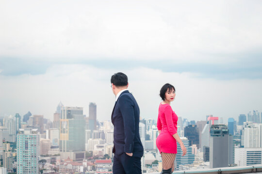 Businessman in suit and attractive woman in red dress walking on street in opposite direction with skyscraper city view, looking and have a crush on each other