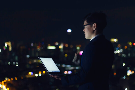 Young Asian Businessman In Suit Using Laptop Computer On The Rooftop With Skyscraper City View At Nigth