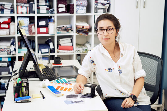 Female fashion designer holding color samples choosing fabric textile at workplace, dressmaker or tailor working at desk pointing at set palette making choice selection           