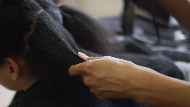 Hands blow-drying afro hair on a young mixed race child